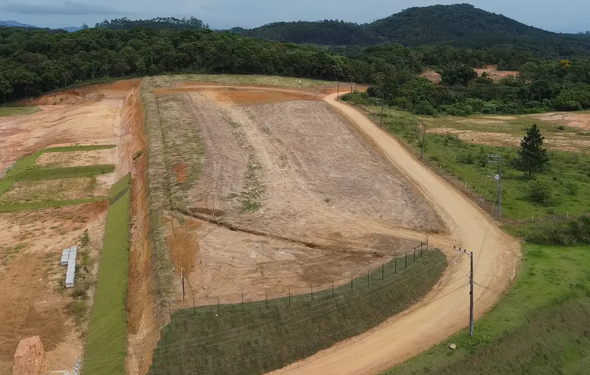 Vista aérea do platô terraplanado, com o talude gramado e o gradil acompanhando a divisa